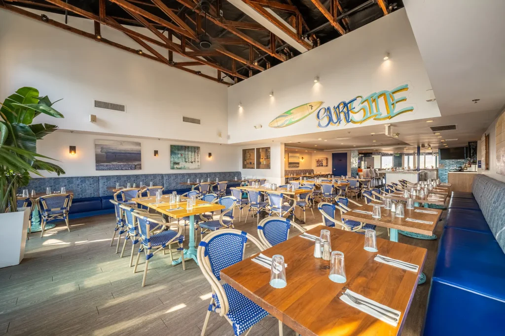Spacious dining room with blue accents, wood tables, and “Surfside” mural at Seaside on the Pier.
