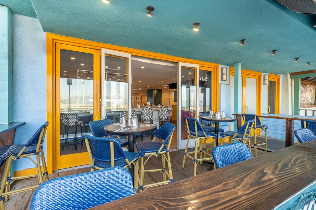 Outdoor patio with blue chairs and yellow-framed doors overlooking the pier at Seaside on the Pier.