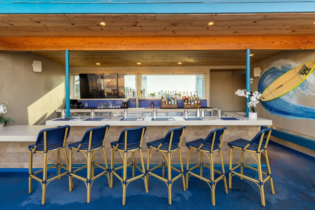 Open-air bar with surfboard mural and high-top seating at Seaside on the Pier.